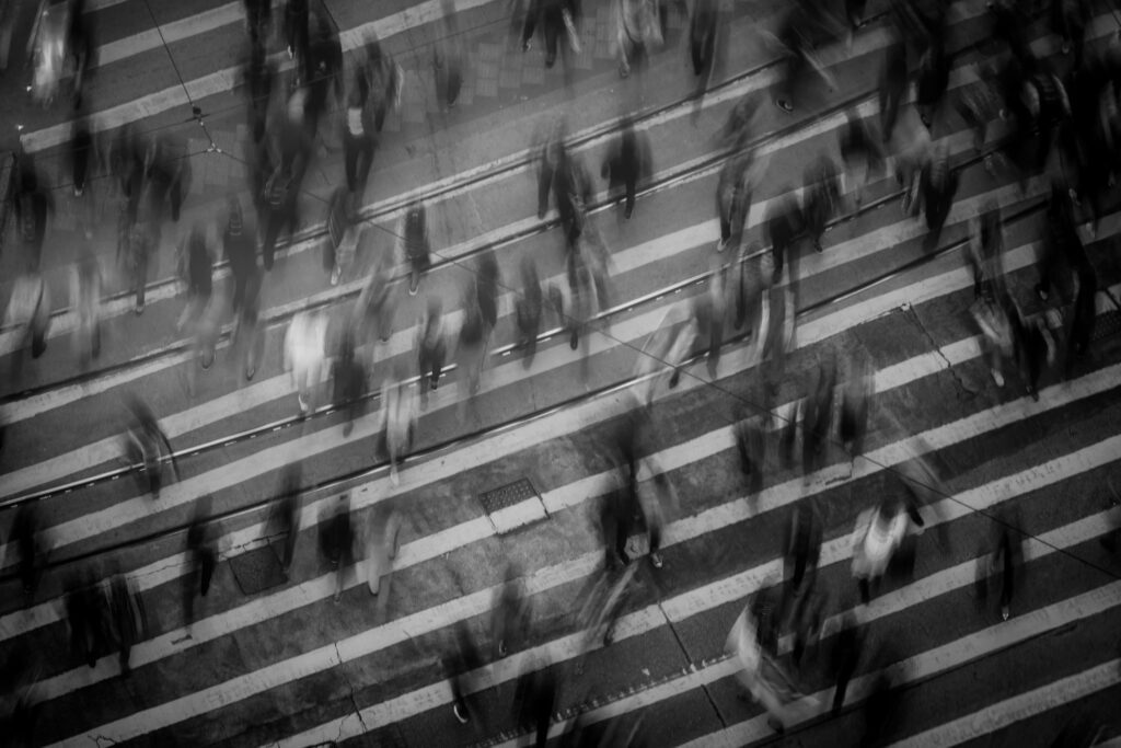 A black and white photo of people walking rapidly across a crossing.