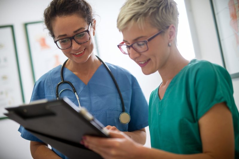Close up of a two cheerful smiling professional female doctors with stethoscope looking at the clipboard of a patient.